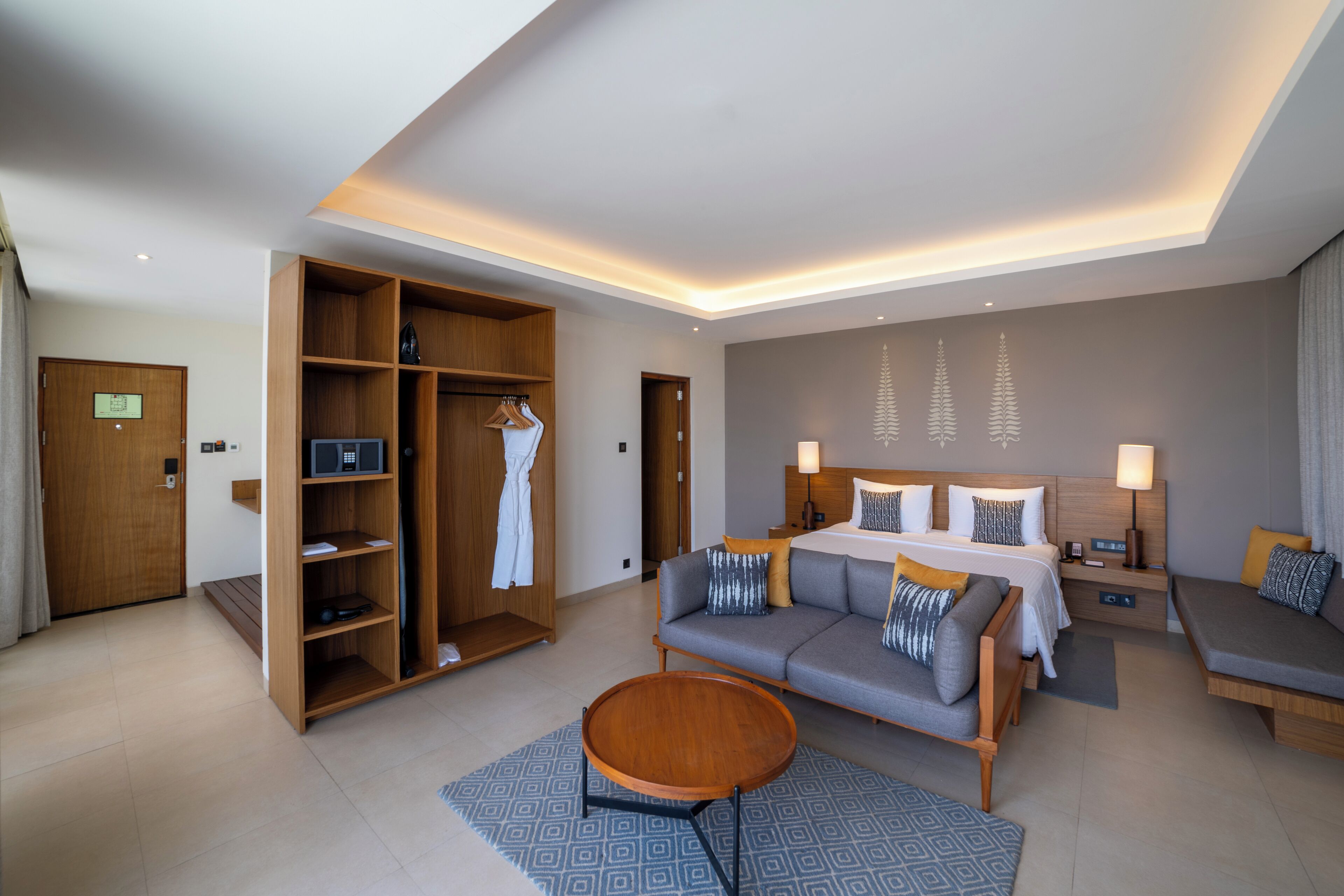 Ett modernt hotellrum med en stor säng, en soffa, ett soffbord, en garderob och ett skrivbord med en lampa.