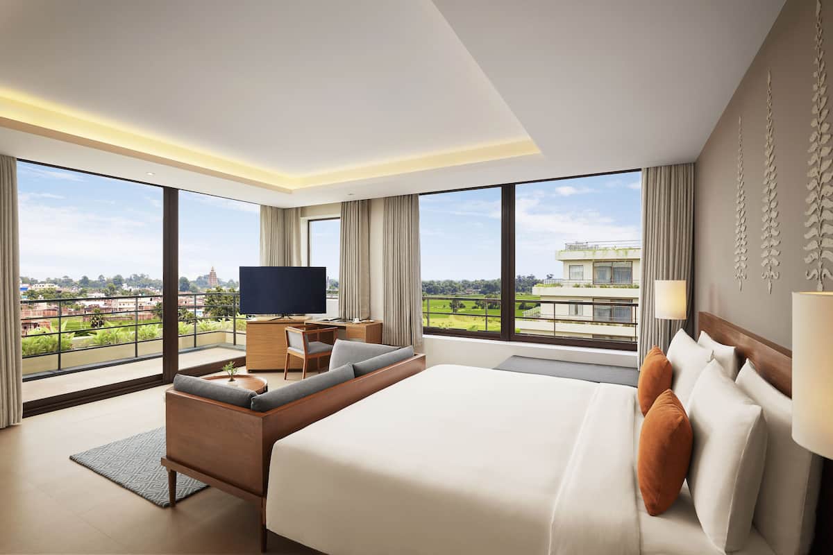 Een moderne hotelkamer met een groot bed, een zithoek, een bureau met een televisie en een balkon met uitzicht over de stad.