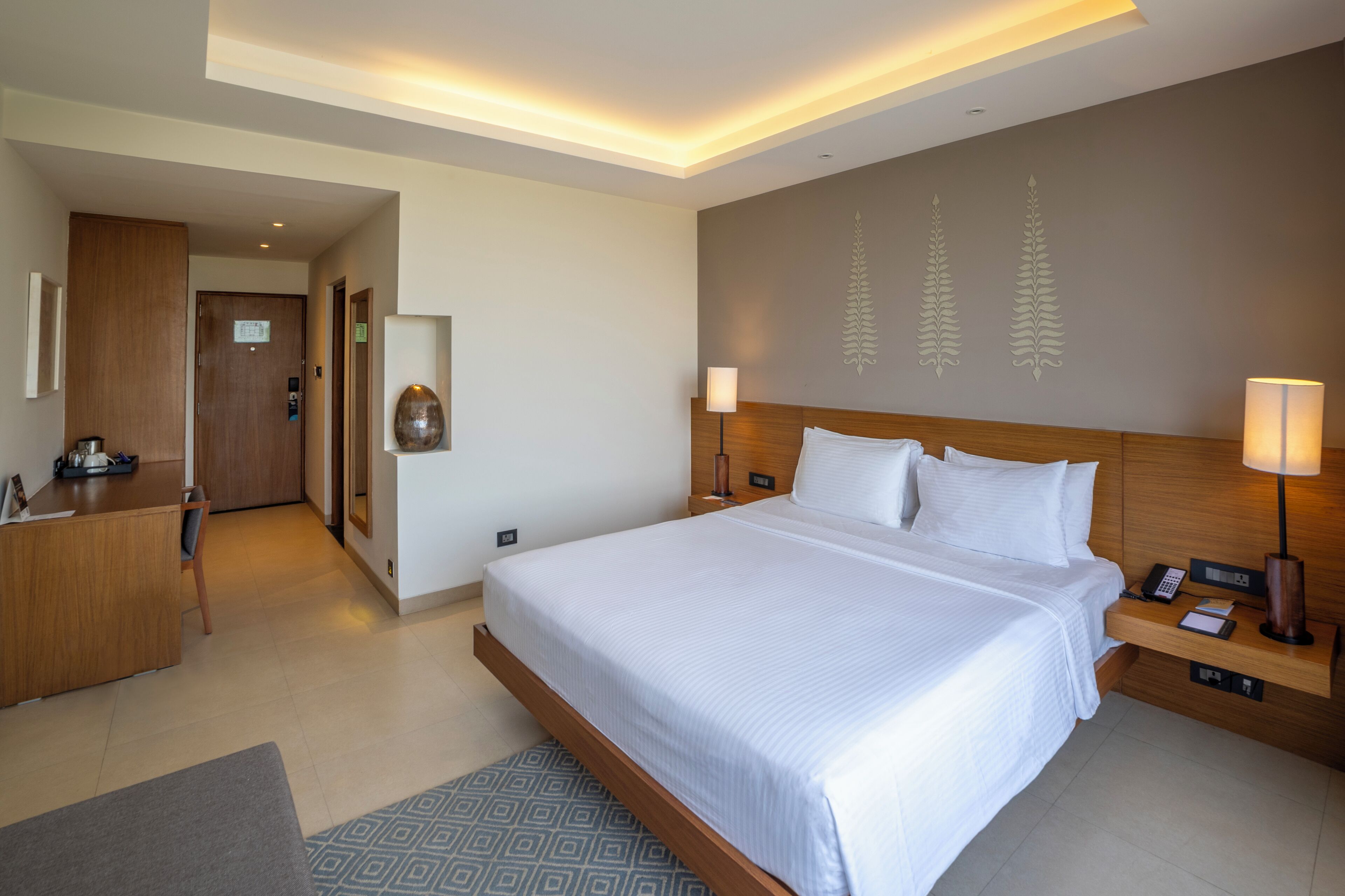 Una habitación de hotel moderna con una cama grande, mesitas de noche, un escritorio y una zona de recepción.