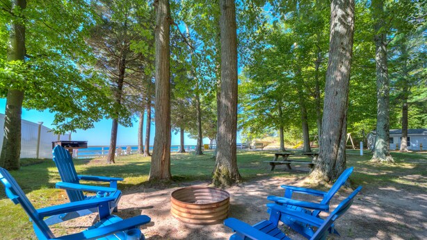 A campground with blue Adirondack chairs, a fire pit, and picnic tables.