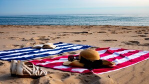 A beach with a striped towel, a hat, and sandals on the sand.