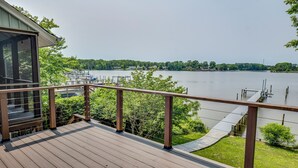 A wooden deck with a railing overlooking a lake, dock, and greenery. - River Refresh - Waterfront with Spa on Placid Bay (Colonial Beach)