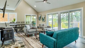A spacious living area with a high ceiling, a ceiling fan, a fireplace, and large windows offering a view of the outdoors. - River Refresh - Waterfront with Spa on Placid Bay (Colonial Beach)