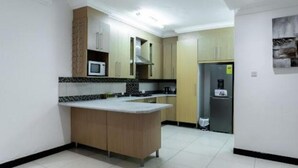 A modern kitchen with a central island, built-in microwave, and stainless steel appliances. - Unit 5, Capella Place (East Legon, Accra)