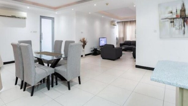 A modern living room with a dining area, a flat-screen TV, and a sofa. - Unit 5, Capella Place (East Legon, Accra)