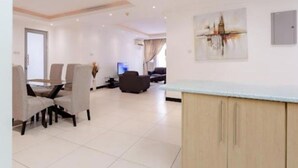 A modern living room with a dining area, a flat-screen TV, and a painting on the wall. - Unit 5, Capella Place (East Legon, Accra)