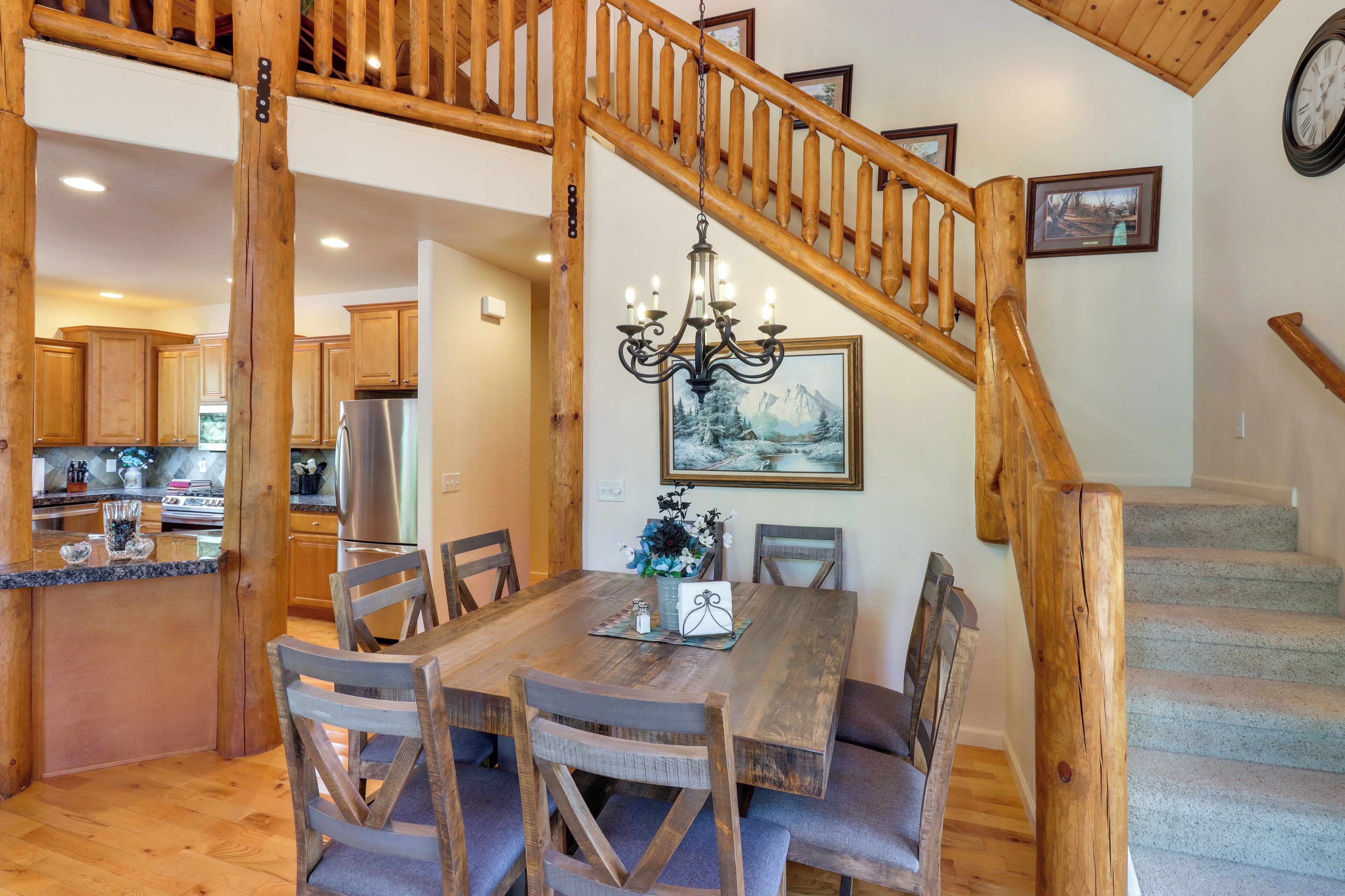 A wooden dining table with chairs, a chandelier, and a staircase with wooden railings.