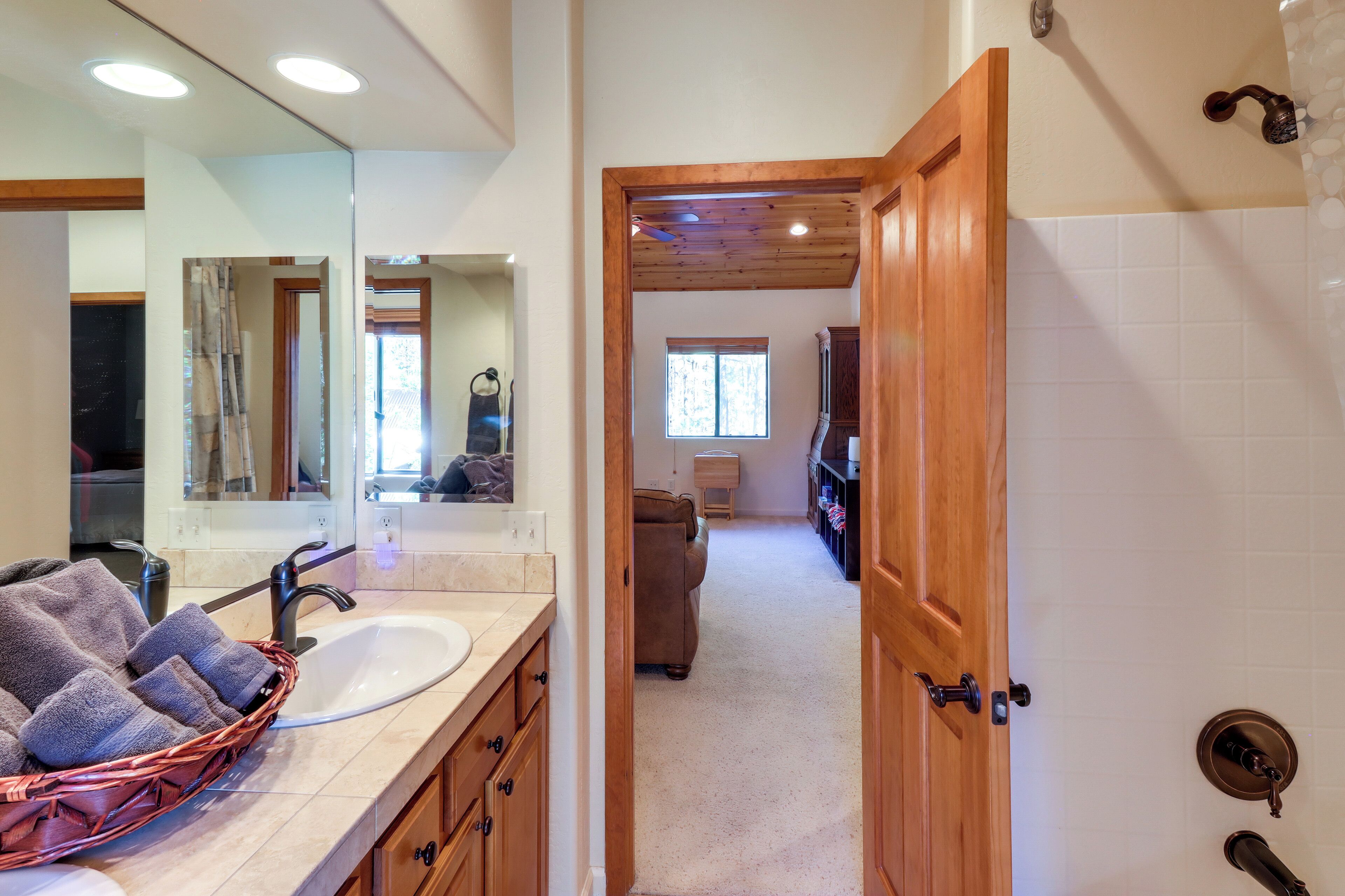 A bathroom with a large mirror, a sink, and a wooden door leading to a hallway.
