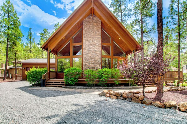 A lodge with a stone chimney, wooden exterior, and a gravel driveway surrounded by trees.
