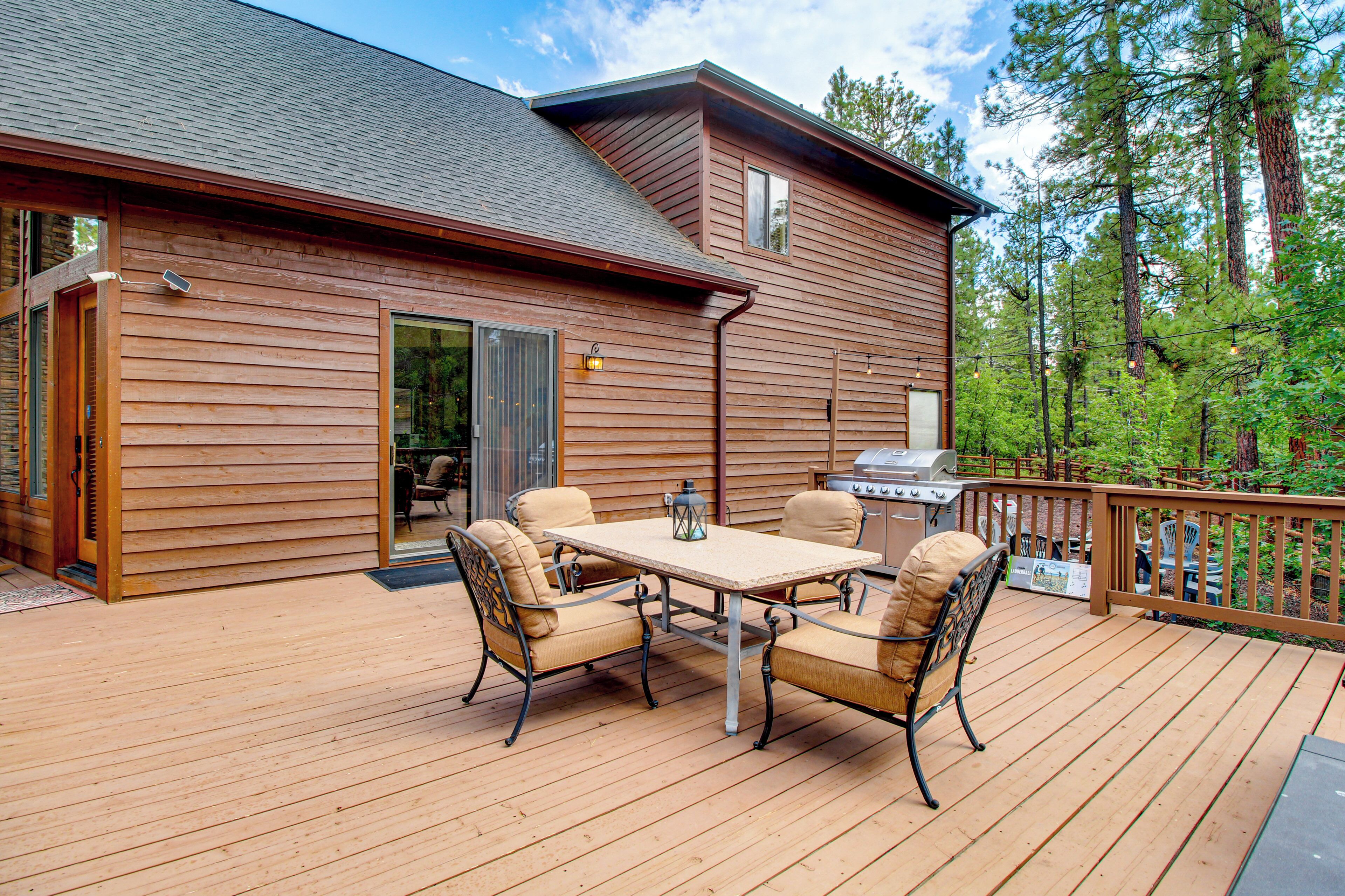 A wooden deck with a table and chairs, a grill, and a view of trees.