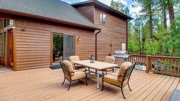 A wooden deck with a table and chairs, a grill, and a view of trees.
