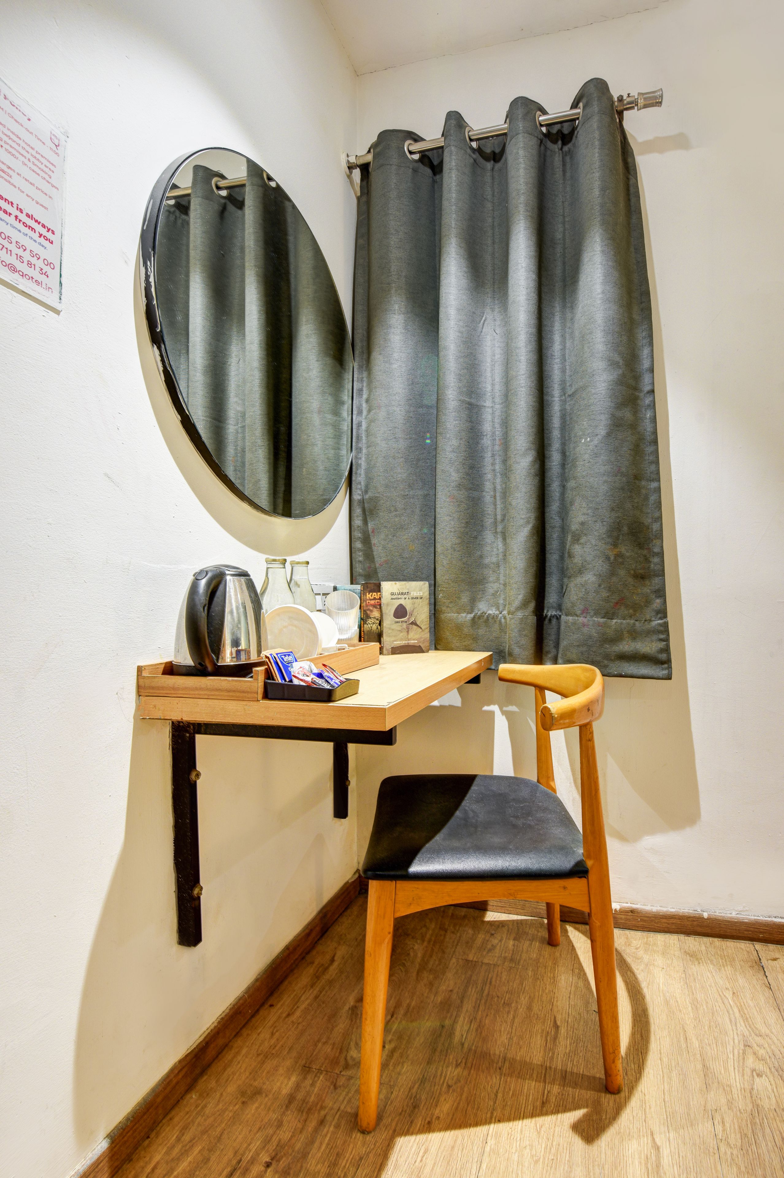 Una stanza piccola con una scrivania in legno, una sedia, uno specchio e una finestra con tende.