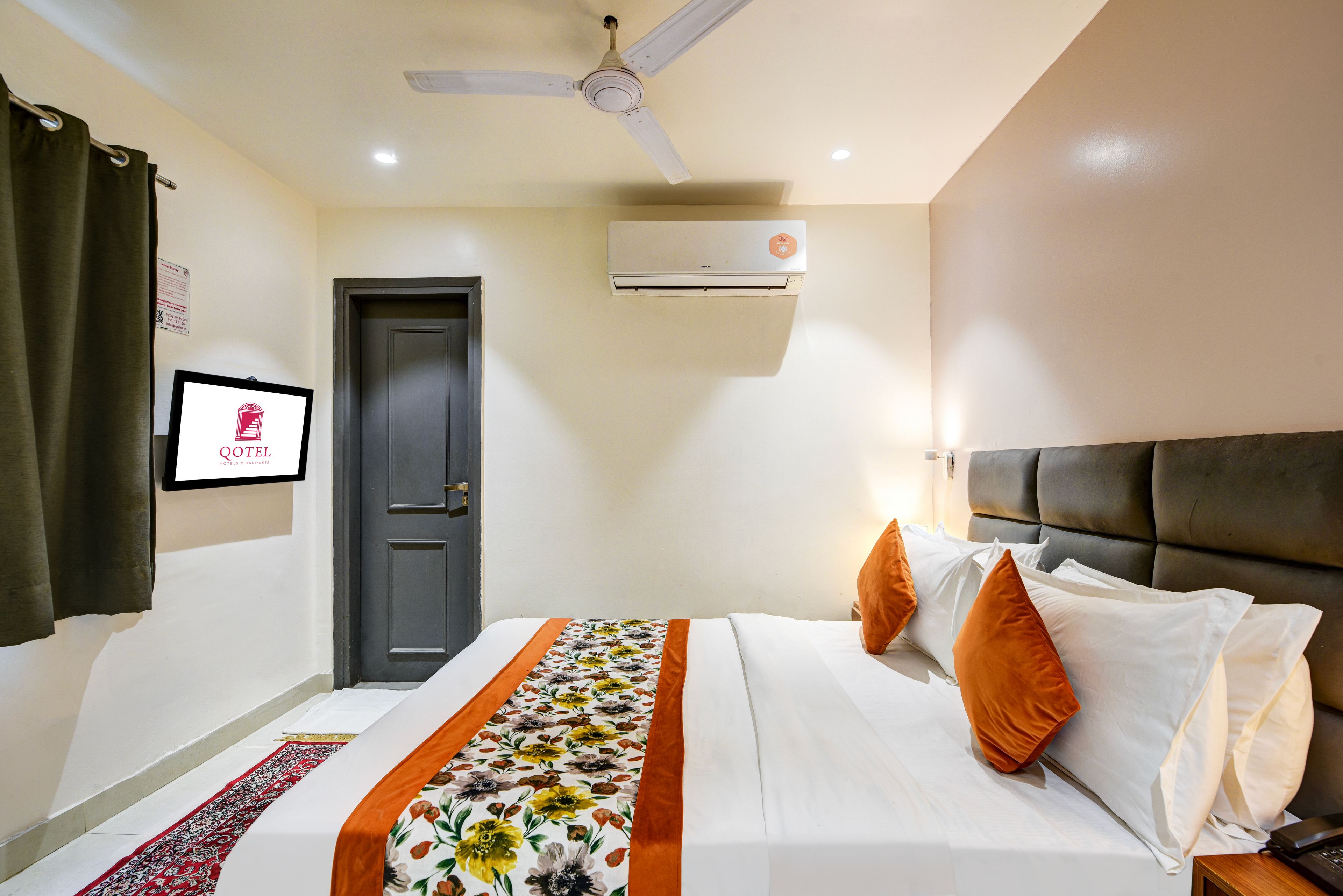 A hotel room with a bed, a ceiling fan, an air conditioning unit, a door, and a framed sign on the wall.