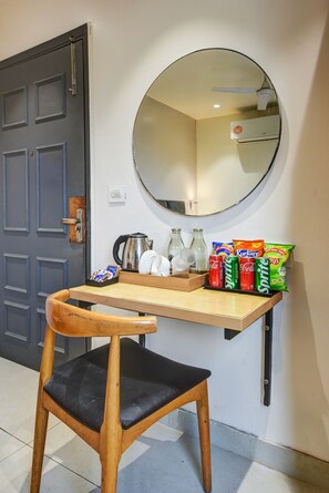 A small kitchenette with a wooden table, a chair, a kettle, and various snacks.