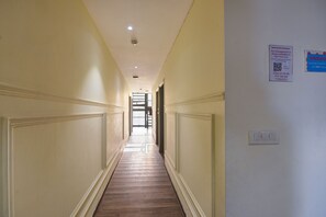 A hallway with a wooden floor and cream-colored walls, leading to a door at the end. - Qotel Hotel IP Residency  (New Delhi)