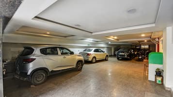 Ett parkeringsgarage med flera parkerade bilar, en utgångsskylt och en grön soptunna.
