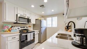 A modern kitchen with white cabinets, stainless steel appliances, a built-in oven, a microwave, a refrigerator, a coffee maker, and a sink. - Scottsdale Vacation Rental: 1 Mi to Old Town! (Scottsdale)