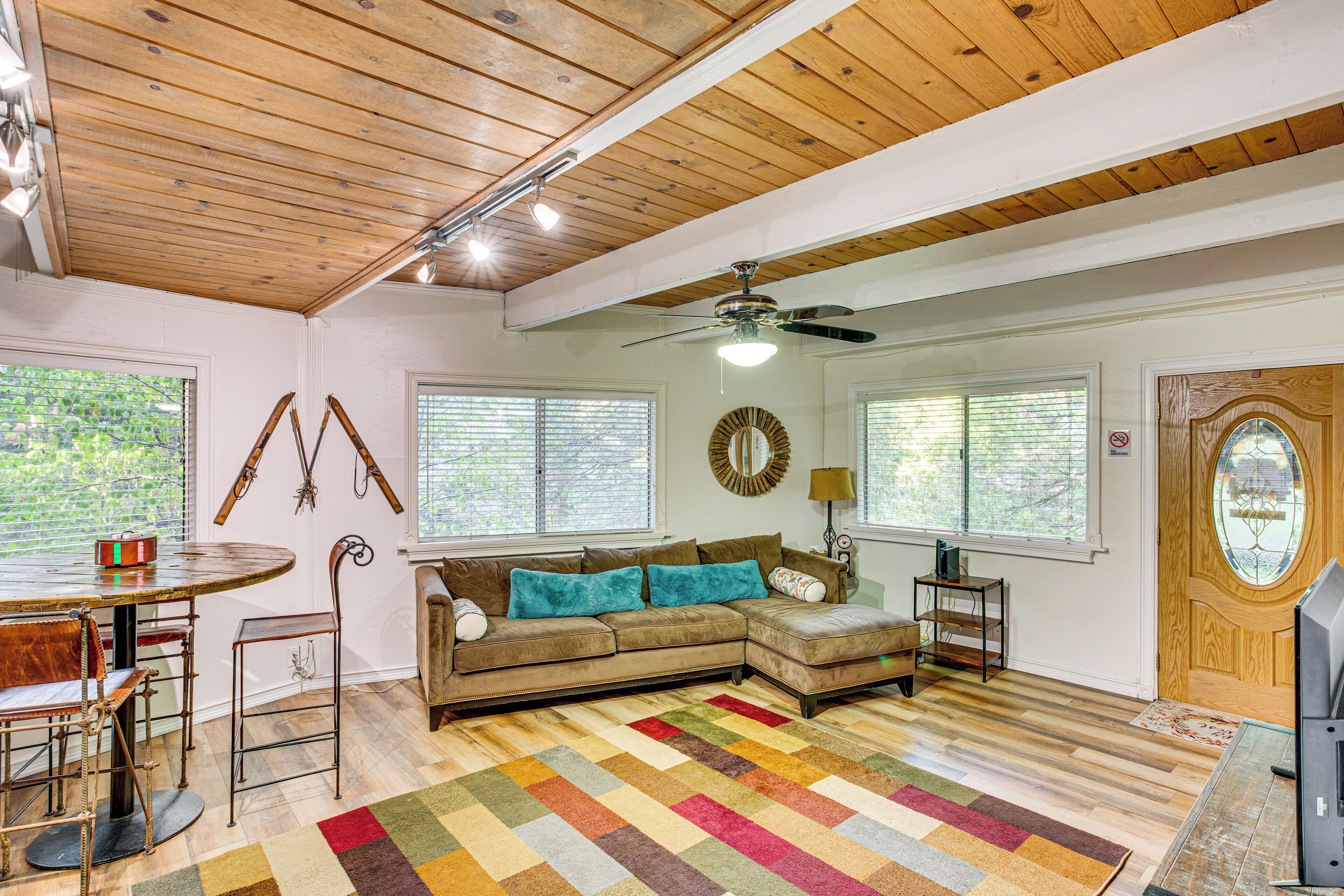 A cozy living room with a sectional sofa, a wooden ceiling, and a colorful rug.