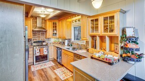A kitchen with wooden cabinets, a stainless steel sink, and a countertop with various food items. - 2 Mi to Skypark at Santa's Village: Family Cabin (Lake Arrowhead)