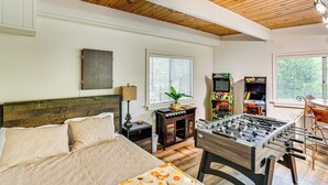 A bedroom with a bed, a wooden ceiling, a window, a table with a plant, and a foosball table. - 2 Mi to Skypark at Santa's Village: Family Cabin (Lake Arrowhead)