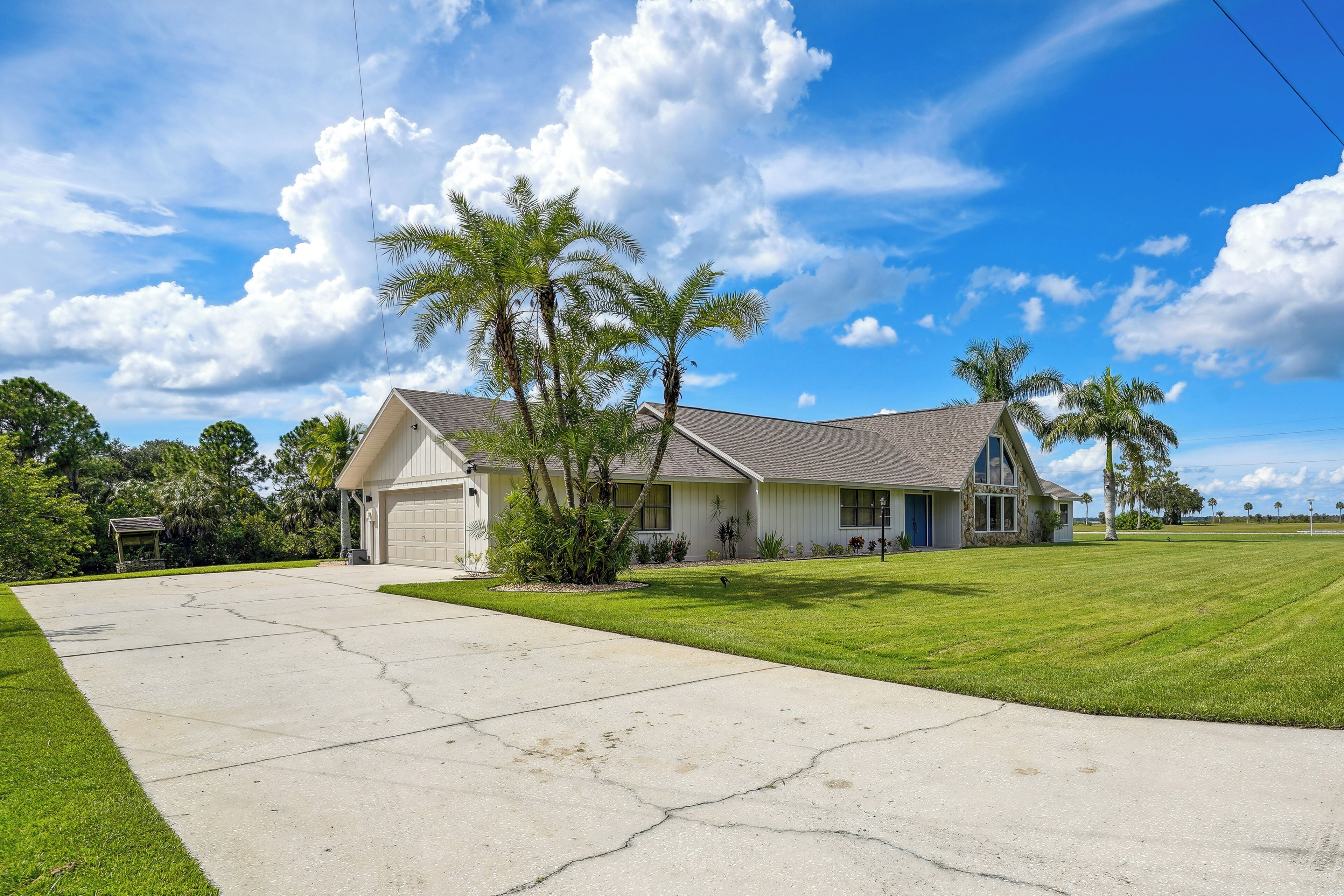 A single-story house with a garage, a well-maintained lawn, and palm trees.