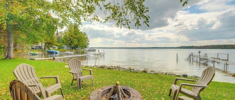 A lakeside outdoor seating area with Adirondack chairs and a fire pit.