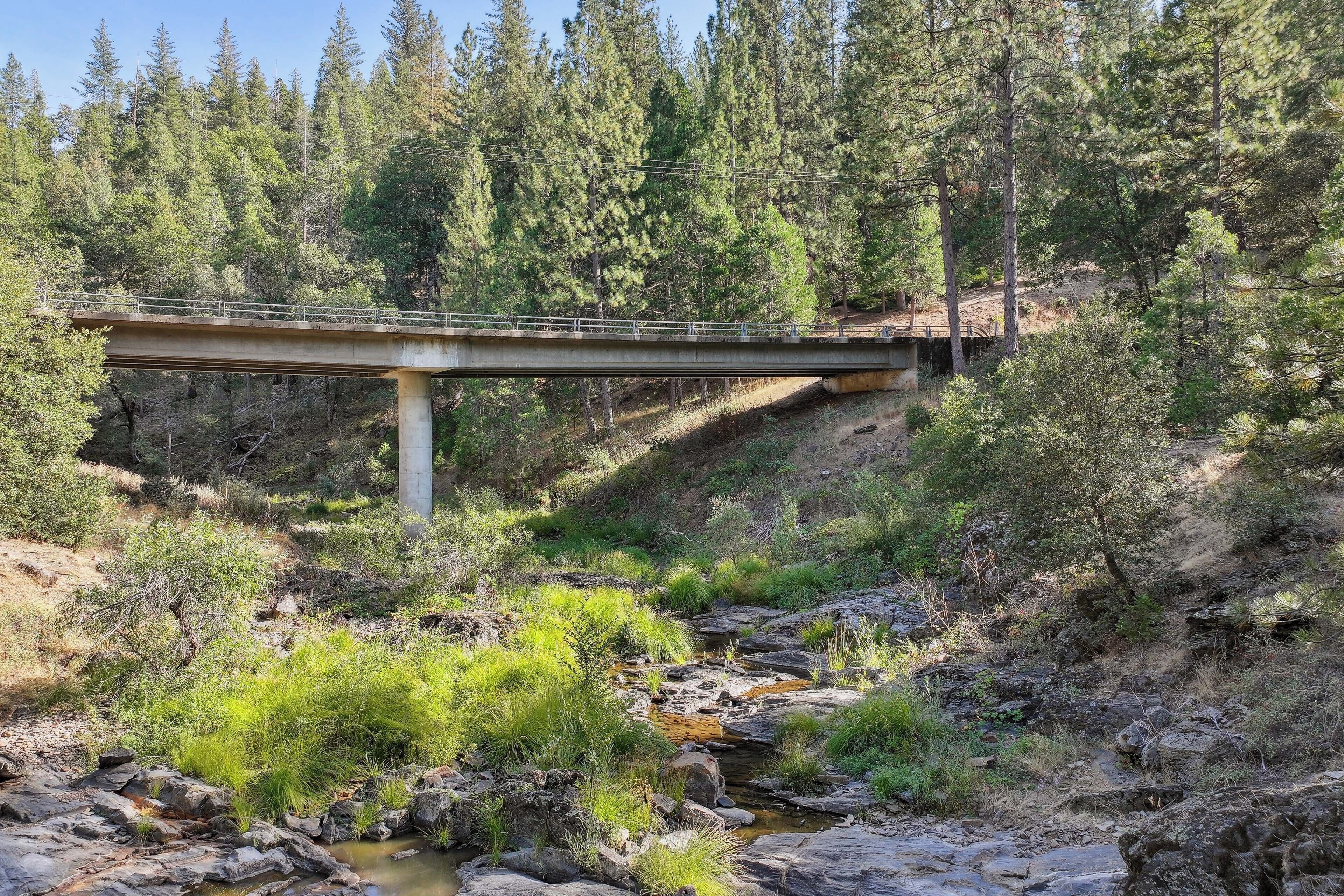 A concrete bridge over a rocky stream in a forested area.