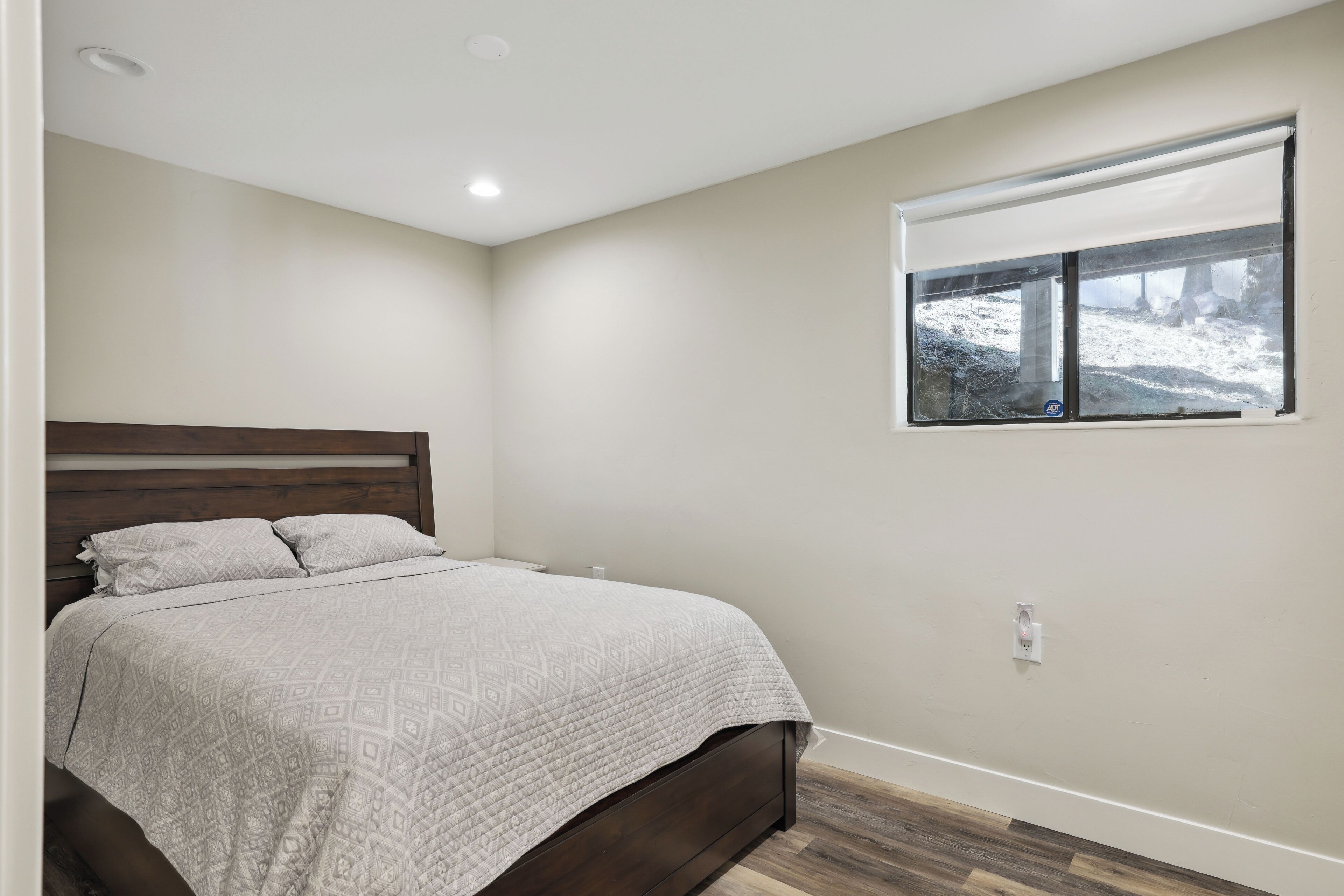 A bedroom with a bed, a window with a view of a snowy landscape, and a wooden floor.