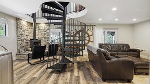 A spacious living room with a spiral staircase, a stone wall, a fireplace, and a leather sofa.