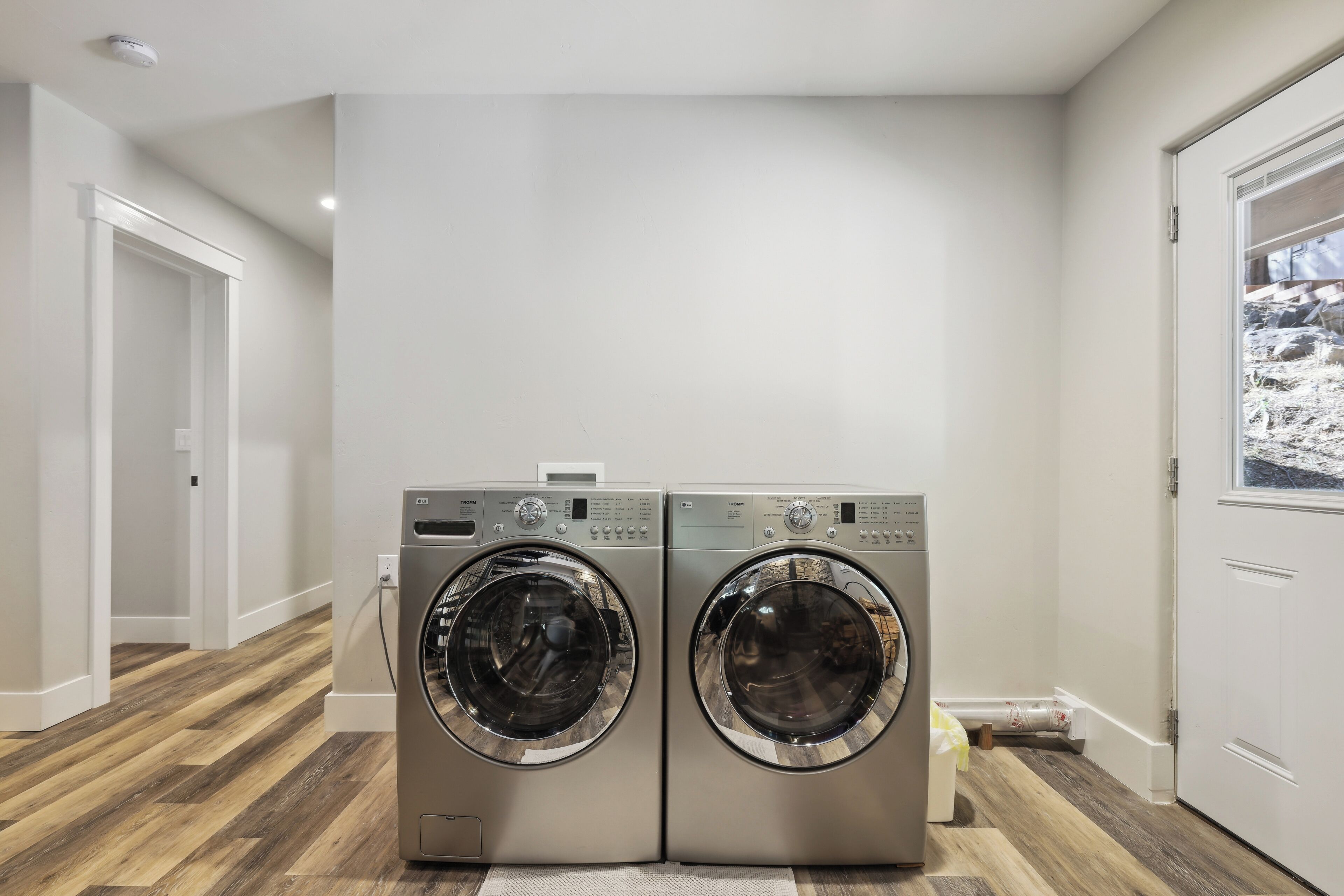 A laundry room with two front-loading washing machines, wooden flooring, and a white door with a window.