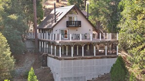 A two-story wooden cabin with a balcony, surrounded by dense forest.