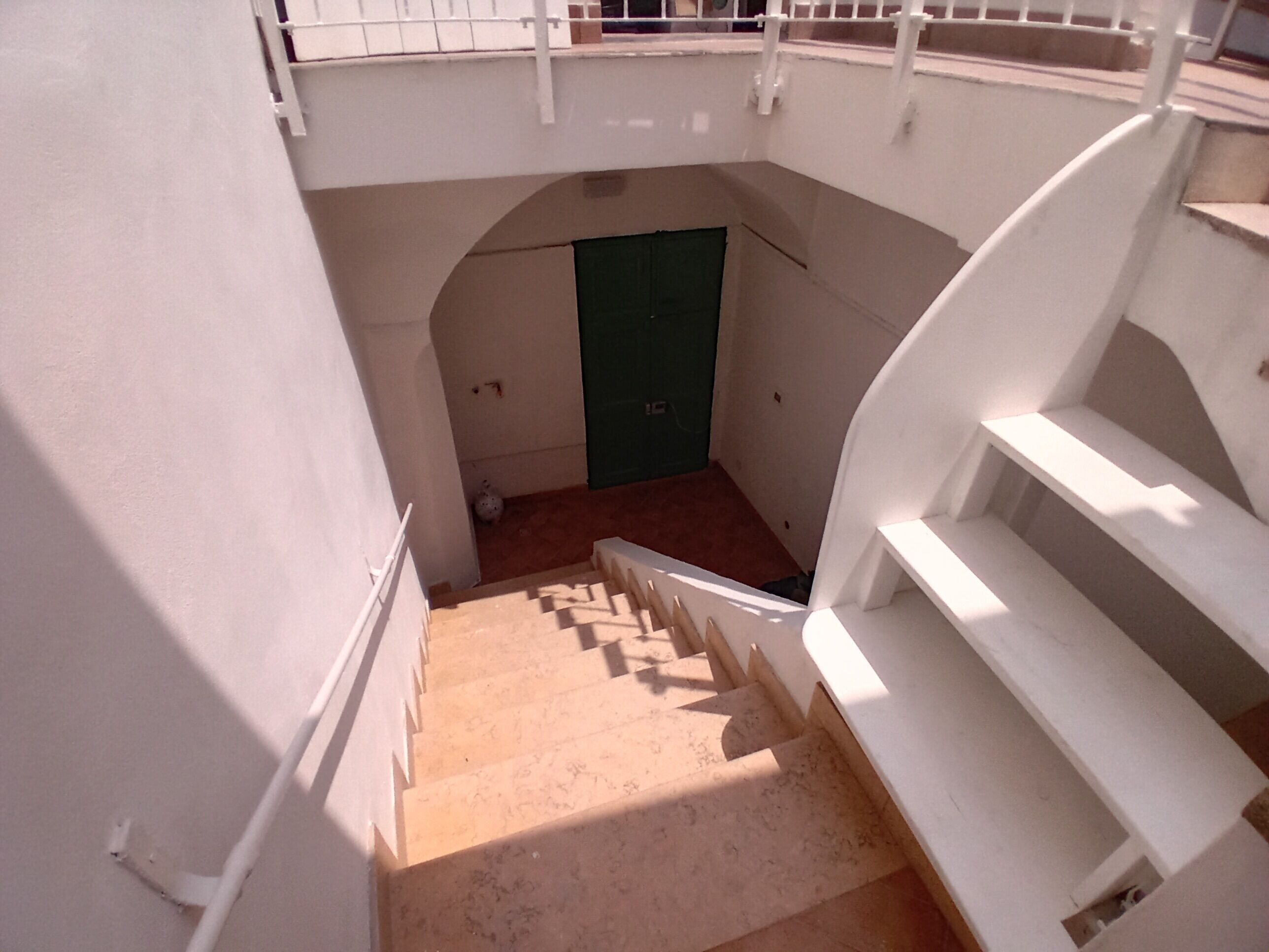 Una escalera conduce a una puerta verde, paredes blancas y una barandilla blanca.