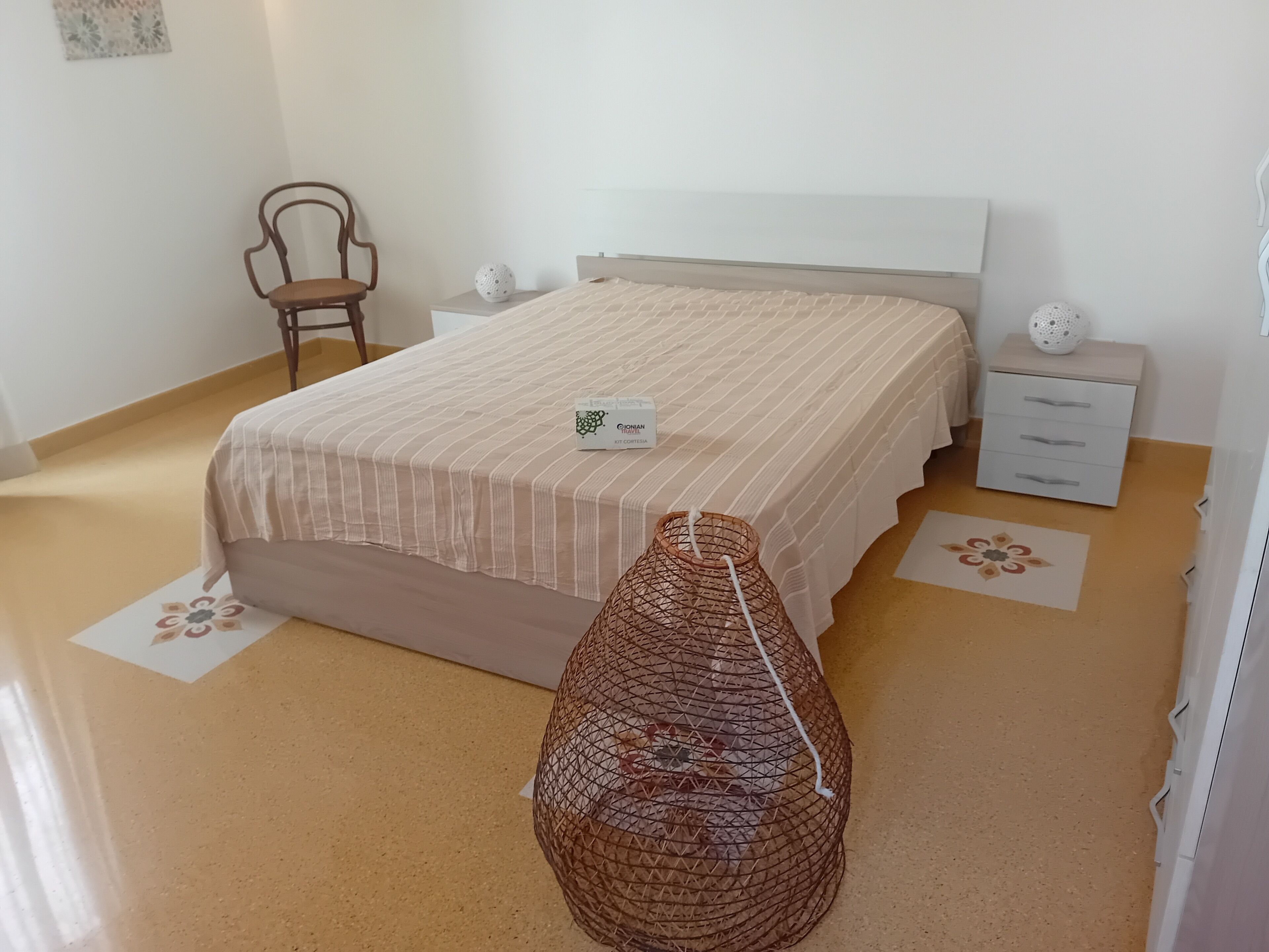 Ein ordentlich eingerichtetes Schlafzimmer mit einem Bett, Nachttischen, einem Stuhl und einem dekorativen Korb.