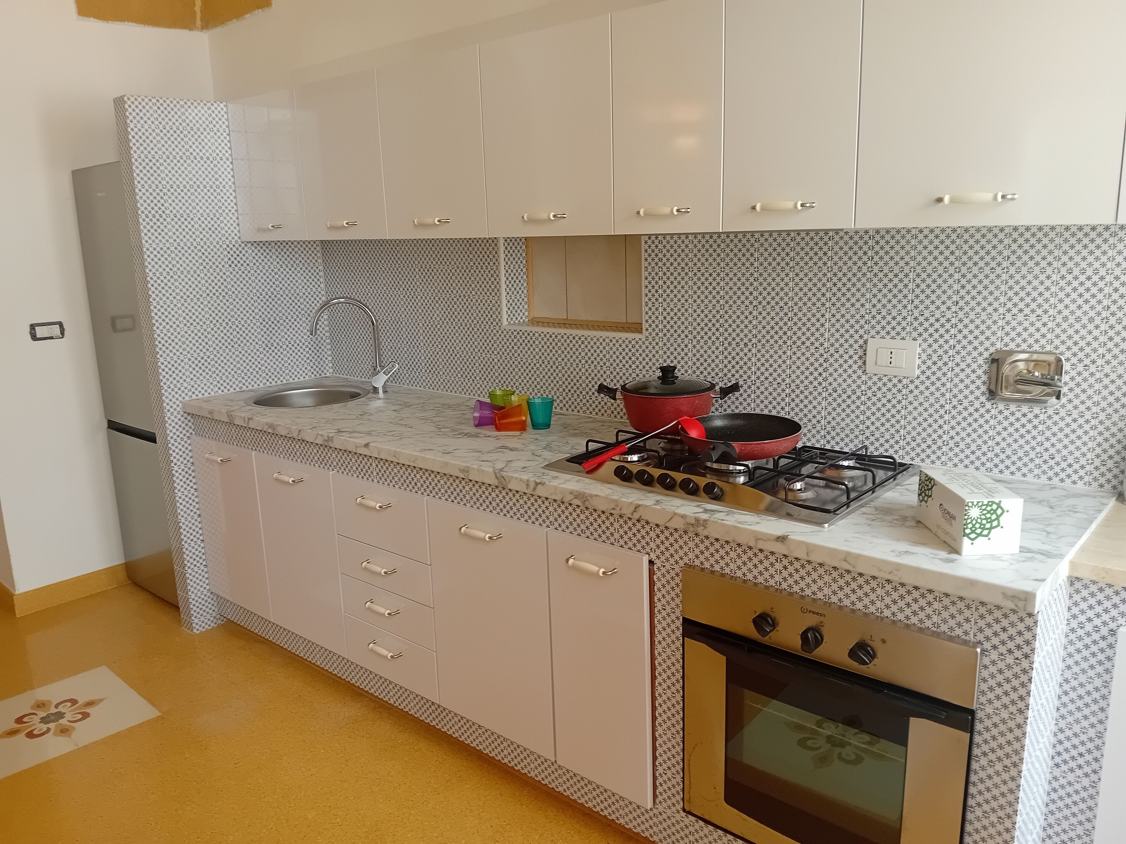 Una cocina compacta con gabinetes blancos, encimera de mármol, cocina a gas, una olla roja y horno empotrado.