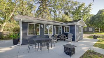 A house with a patio area featuring a table and chairs, surrounded by trees.