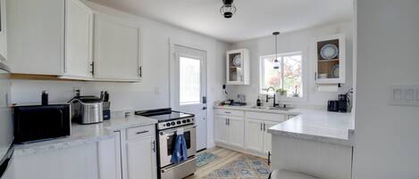 A modern kitchen with white cabinets, a stove, microwave, and a sink.