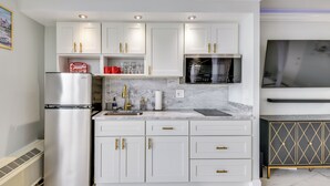 A modern kitchen with white cabinets, gold handles, a stainless steel refrigerator, a microwave, and a marble countertop. - Cozy Florida Getaway w/ Pool Access & Ocean Views! (Daytona Beach)