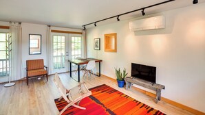 A modern living room with a wooden floor, a red and black striped rug, a television on a wooden stand, a potted plant, and a dining area with a table and chairs.