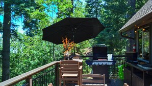 An outdoor deck with a table, chairs, a grill, and an umbrella. - Cozy & Chic Lake Arrowhead Cabin w/ Deck! (Lake Arrowhead)