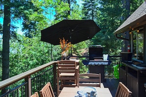 Um deck externo com mesa, cadeiras, churrasqueira e guarda-sol.