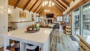 A spacious kitchen with a large island, a stone fireplace, and a dining area with a view. - Cozy & Chic Lake Arrowhead Cabin w/ Deck! (Lake Arrowhead)