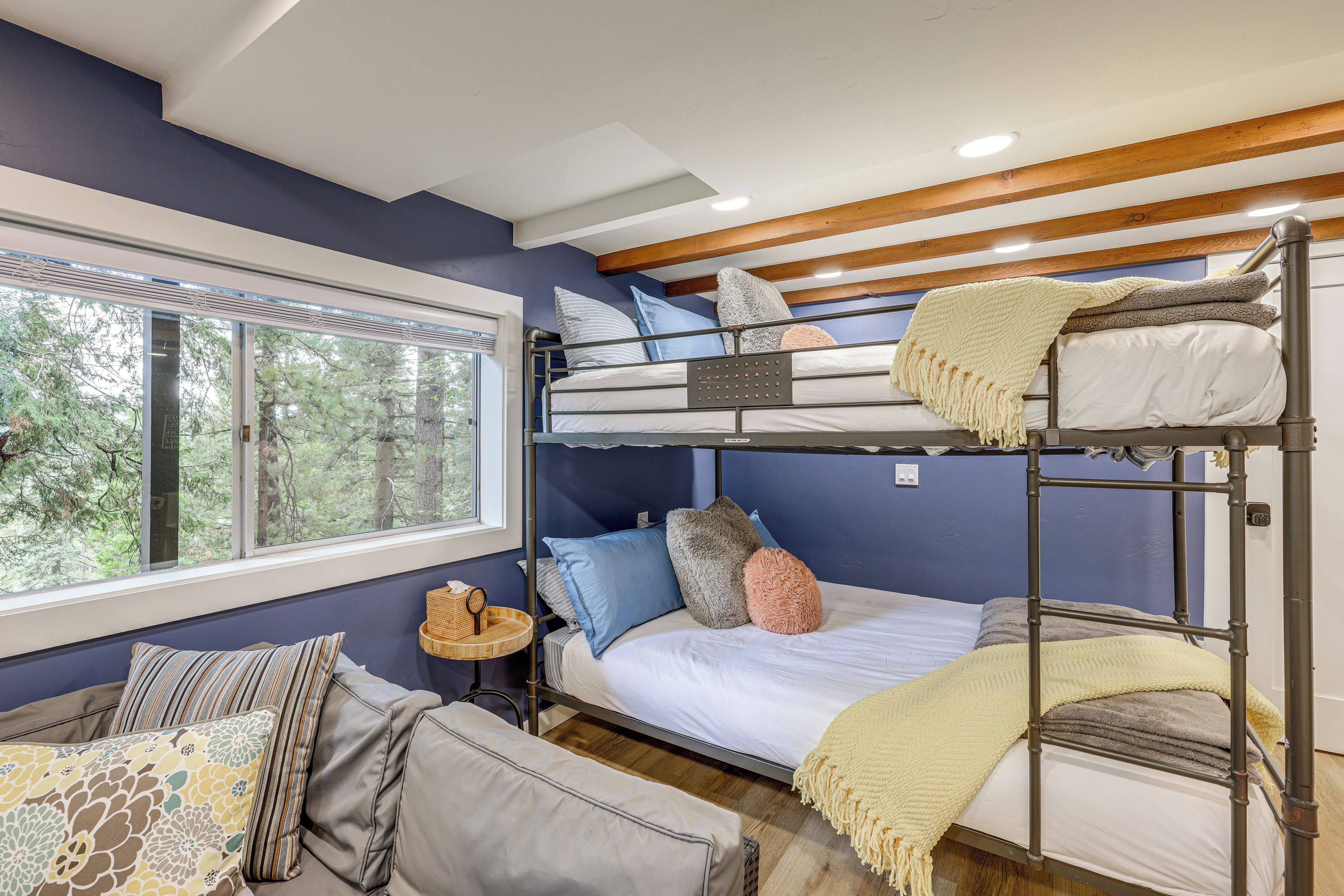 A bunk bed room with a window, a small table, and a sofa.