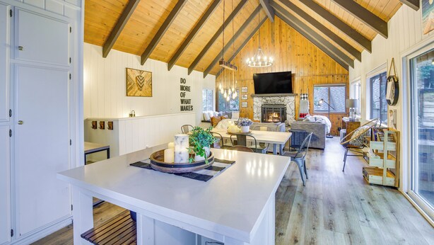 A spacious kitchen with a large island, wooden ceiling beams, and a stone fireplace. - Cozy & Chic Lake Arrowhead Cabin w/ Deck! (Lake Arrowhead)