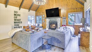 A cozy living room with a fireplace, comfortable seating, and a large TV. - Cozy & Chic Lake Arrowhead Cabin w/ Deck! (Lake Arrowhead)