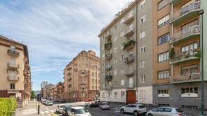 Vista de la calle en un barrio residencial con edificios de apartamentos de varios pisos, coches aparcados y cielo despejado.