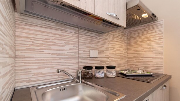 Una cocina moderna con un lavamanos de acero inoxidable, una estufa empotrada y un microondas. Hay tres frascos de especias en la encimera.
