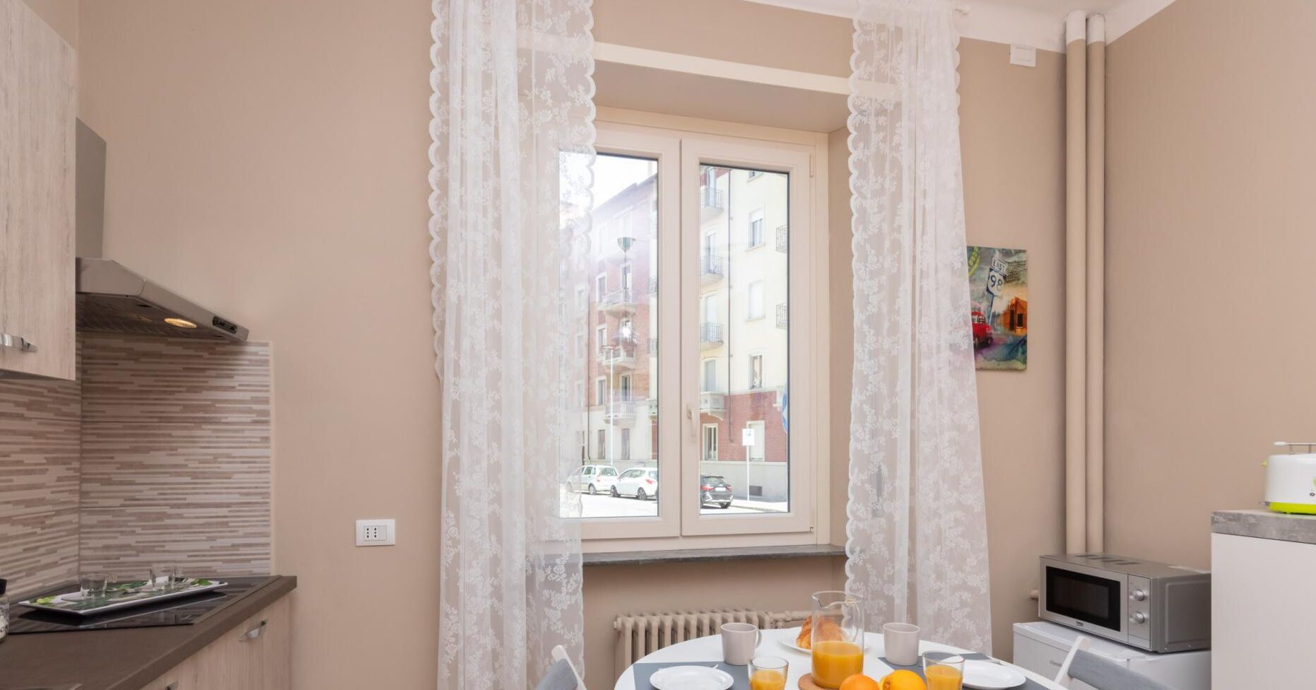 A kitchen with a window, a microwave, and a dining table set with orange juice.