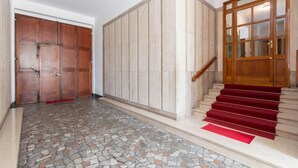 Un pasillo con suelo de baldosas, una puerta de madera, un panel de pared de madera y una escalera con alfombra roja.