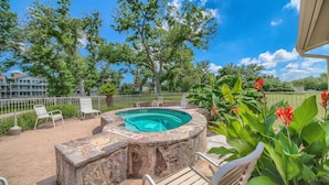 A hot tub with a stone exterior, surrounded by lounge chairs and greenery.