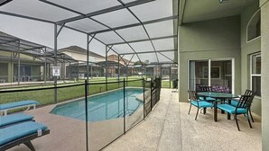 A covered outdoor pool area with a patio table and chairs, surrounded by a fence. - 4 Bed 3 Bath In A Gated Community With Pool 4 Bedroom Villa by RedAwning (Kissimmee)